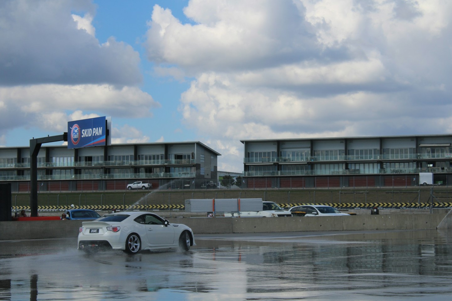 White sports car drifting across a wet training surface.