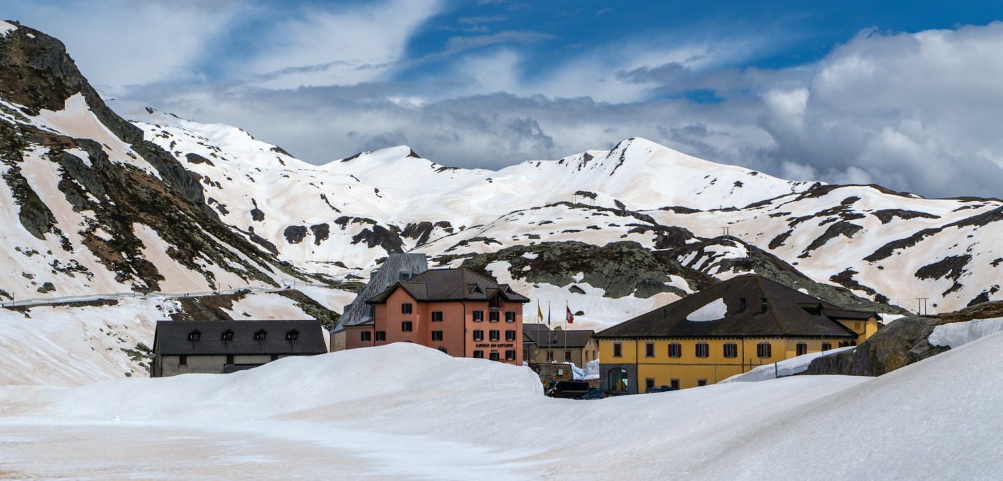 Buildings at the Gotthard Pass summit below rocky mountains with patches of snow.